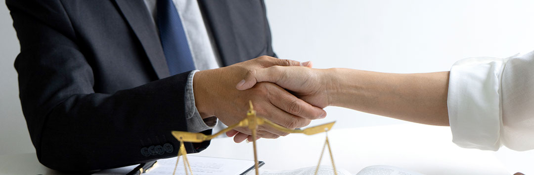 Two hands shaking next to a book and a pair of gold scales