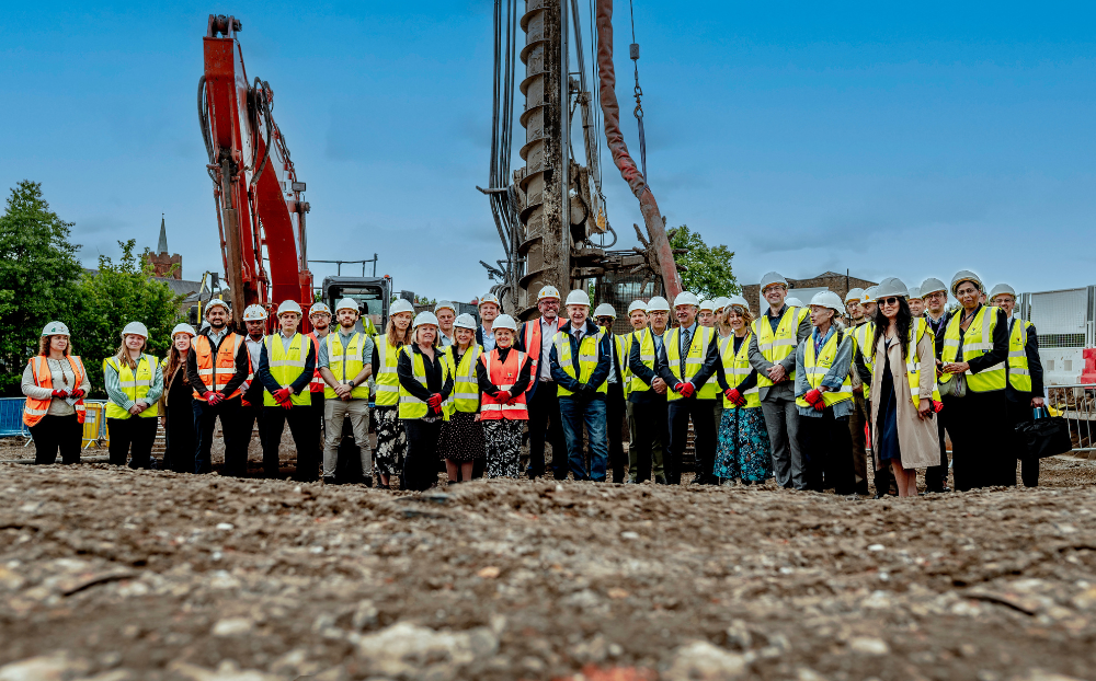 A group of academics and construction staff wearing hard hats at the construction site of the new school of business and management building