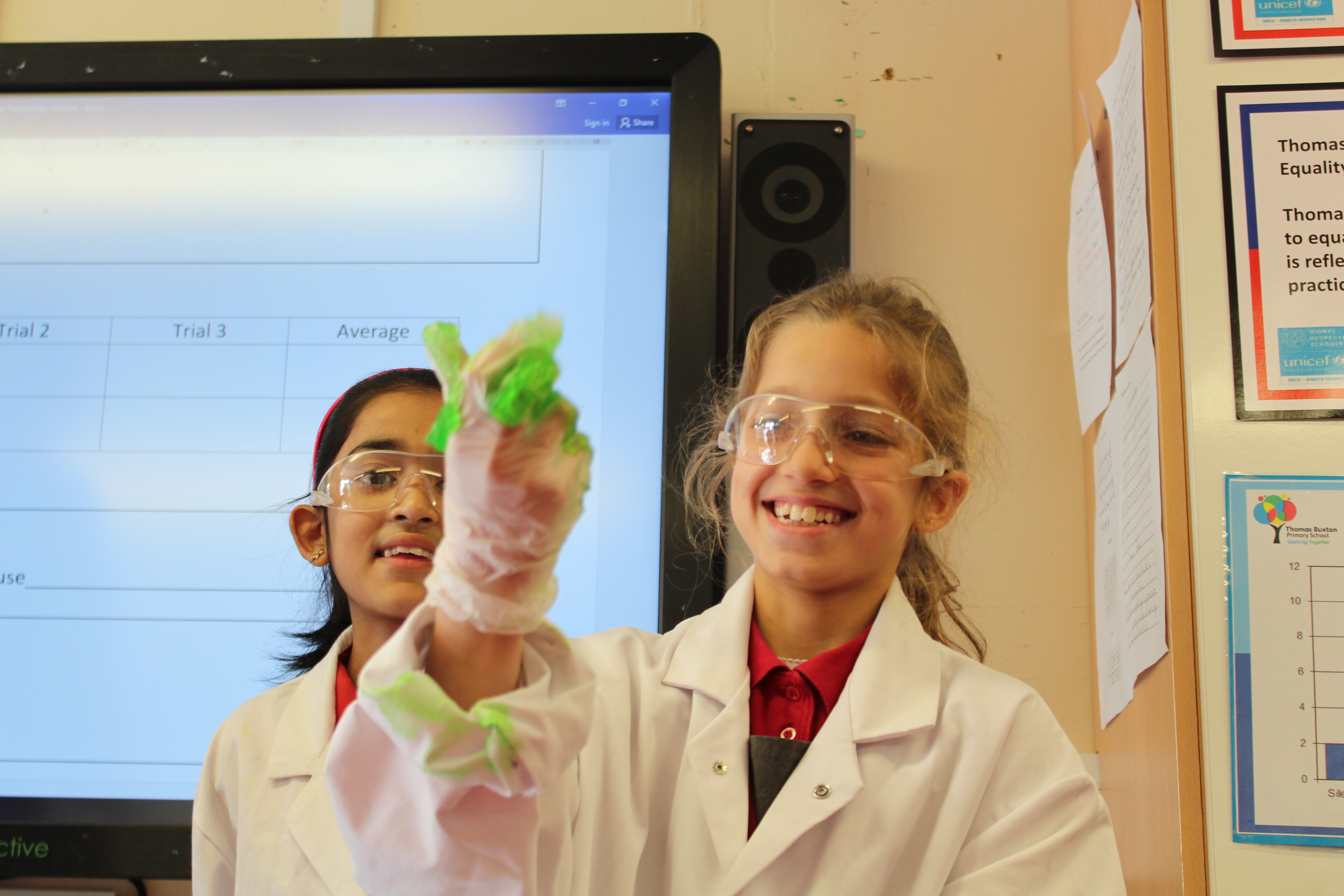 School children in lab coats and safety goggles playing with goo