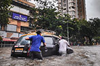 Two men pushing a black car through flood waters