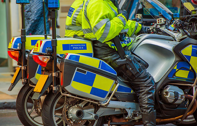 Two London Metropolitan police officers in high-vis jackets sat on parked motorcycles.