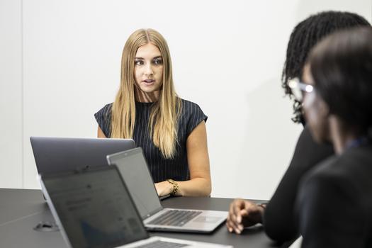 Three women sat in a meeting room with laptops.