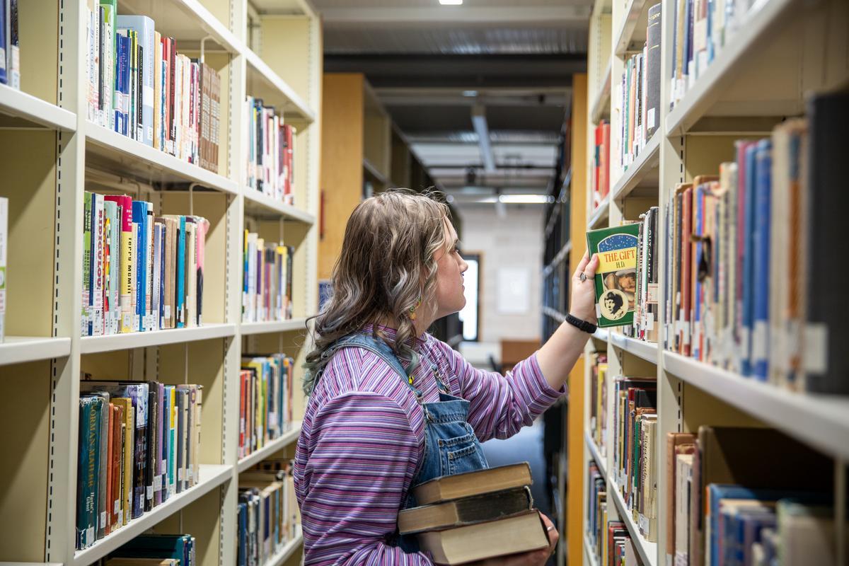Student selecting a book from bookshelves in Mile End Library