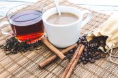 A cup of coffee and a cup of tea with tea leaves and coffee beans on a tablemat