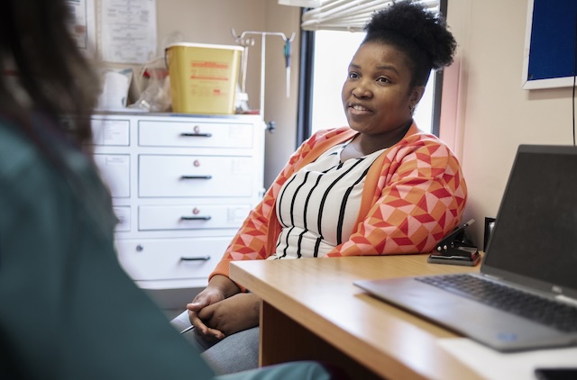 A woman is sitting at a desk speaking to their GP