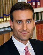 Headshot of Davor Jancic wearing a suit in front of a bookshelf