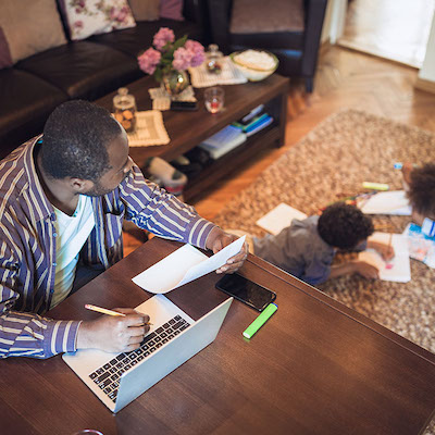 A man working on a laptop with children drawing in the background