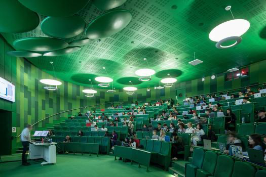 A lecturer in at the front of a large tiered lecture theatre